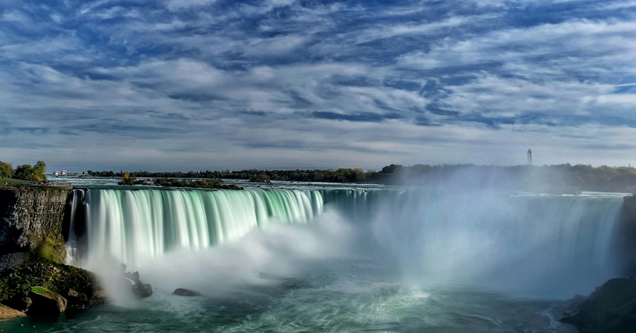 Krachtige waterval met opstijgende mist onder een bewolkte lucht.