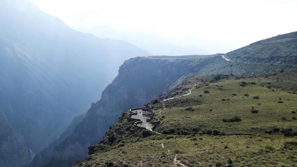 Een uitzichtpunt met golvende platforms op de rand van een steile kloof, met mensen die van het berglandschap genieten.
